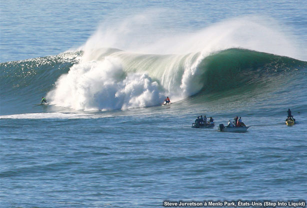photo showing surfers in big waves with small boats beside