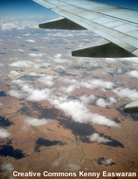 photo of plane wing over cumulus clouds and desert-like terrain