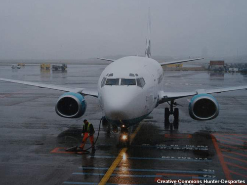 Aeronave comercial estacionada en la terminal bajo una lluvia torrencial. La torre de control apenas se distingue en la distancia.
