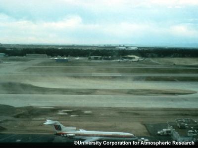 Foto de polvo levantado por el viento sobre las pistas de un aeropuerto detrás de un avión comercial