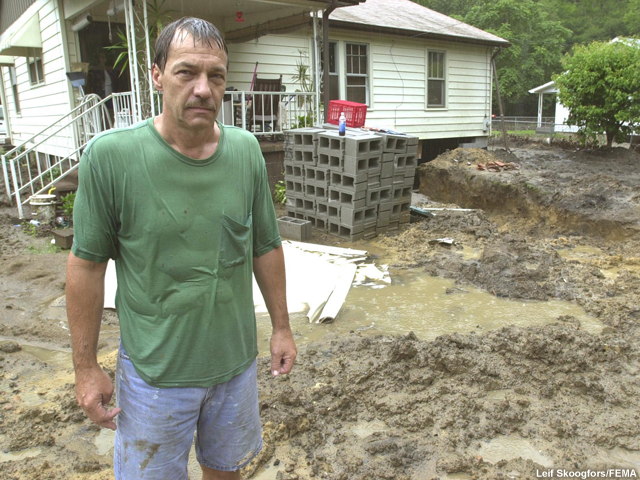 Hombre empapado por la lluvia delante del jardín de su casa, en Virginia Occidental, hecho un barrial por las lluvias que inundaron la zona.