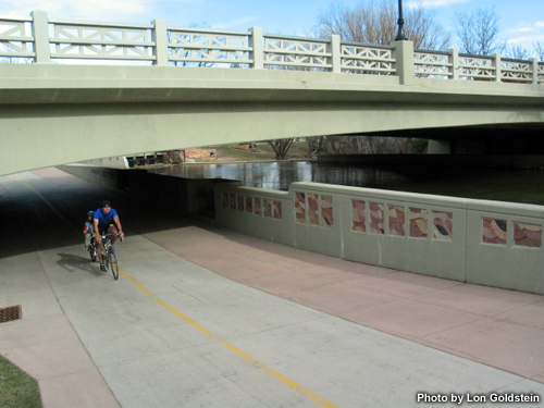 Photo of bike path under bridge by river