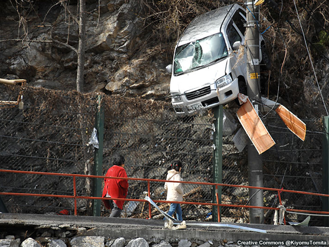 A couple look at a minivan stuck high on a cliff after the 2011 Japan tsunami.