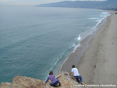 photo of waves at beach and people viewing from high rock