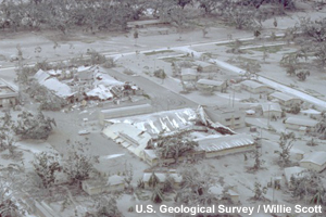 Aerial view of part of Clark Air Base showing buildings and vegetation damaged by tephra after Mt Pinatubo's eruption. Collapsed roofs and buildings, broken trees, tephra covers all in view.