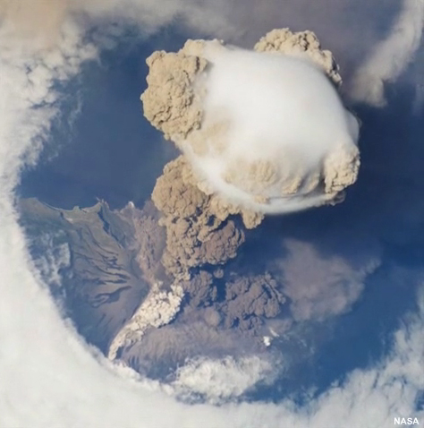 International Space Station view of Sarychev Volcano (Kuril Islands, northeast of Japan) in an early stage of eruption on June 12, 2009.  The ash plume is viewed from above and it has pierced the cloud cover above the volcano.  A pyroclastic flow is visible on the volcano's flank.